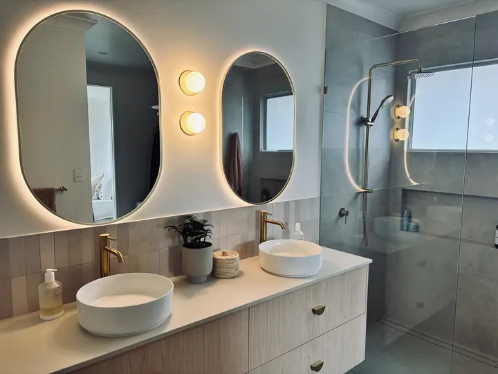 Double vanity with gloss wall tiles beside a walk-in shower with brass fittings