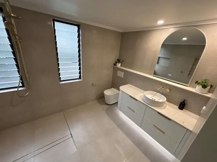 Bathroom with large-format grey wall and floor tiles, an arched mirror and wall-hung toilet
