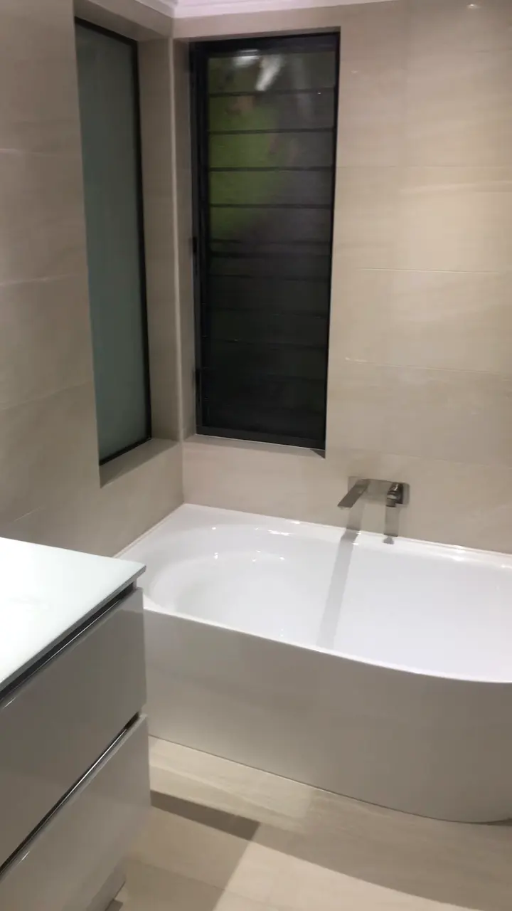 Video walkthrough of a completed bathroom renovation with beige large-format tiles, a corner bath and walk-in shower