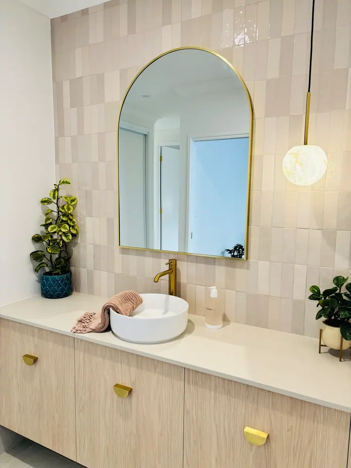 Vanity wall in vertically stacked blush handmade-look tiles with a brass arched mirror