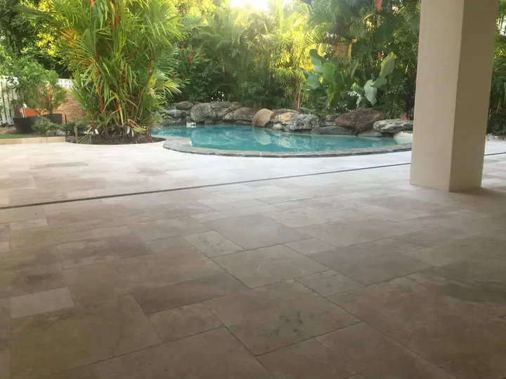 Covered outdoor area with stone-look floor pavers overlooking a lagoon-style pool